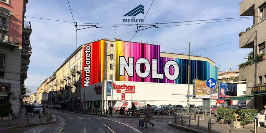 Facciata colorata con la grande scritta NoLo lungo una strada di Milano percorsa dai binari del tram