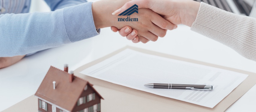 Stretta di mano sopra un contratto con penna e casetta in miniatura: concessione di un mutuo