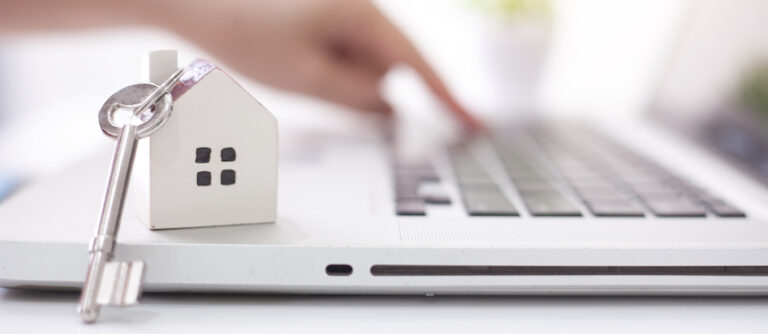 Mani digitano su un portatile accanto a un portachiavi a forma di casa: vendita di un immobile online